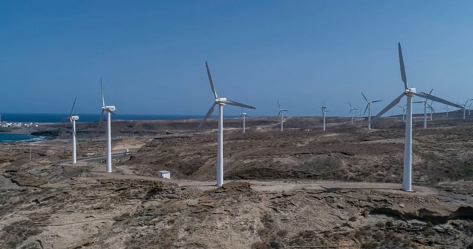 Wind turbines along a bare stretch of coast under a grey sky